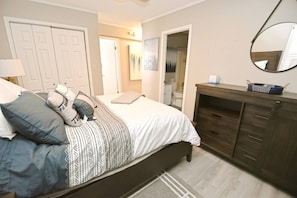 A bedroom with a bed, bedside tables, a dresser, a mirror, and a door leading to a bathroom.