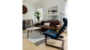 A modern living room with a brown sofa, a blue armchair, a coffee table, a floor lamp, and a bookshelf. - Home Getaway w/ Unique 🔥Fire Pit. Near Napa & SF (Vallejo)