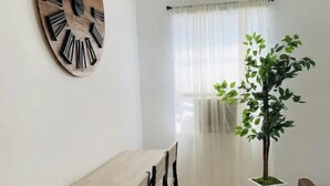 A dining area with a wooden table and chairs, a large wall clock, a potted plant, and a window with sheer curtains. - Home Getaway w/ Unique 🔥Fire Pit. Near Napa & SF (Vallejo)