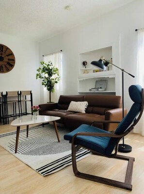 A modern living room with a brown sofa, a blue armchair, a coffee table, a floor lamp, and a bookshelf.