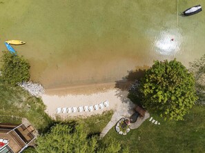 An aerial view of a beach with a wooden deck, lounge chairs, and a small garden area. - *NEW* Lakeside Club - 10 Minutes to Harbor Springs and Petoskey! (Petoskey)