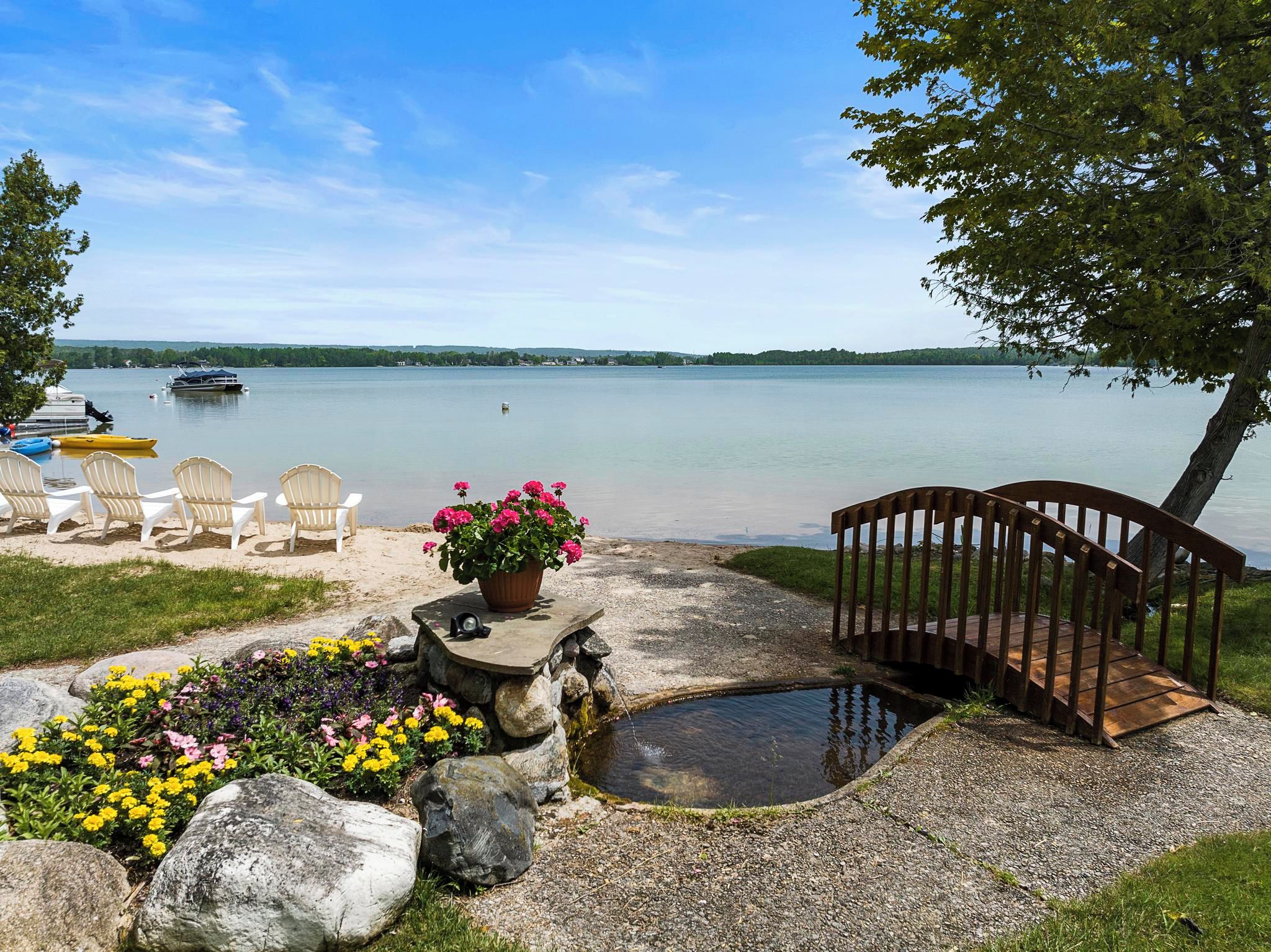 Un patio affacciato su un lago con poltrone Adirondack, una panchina di legno, un vaso di fiori e un piccolo stagno.