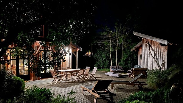 Une terrasse en bois, agréée de mobilier d’extérieur, notamment une table et des chaises, et entourée de verdure.