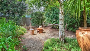 Un jardin avec une table en bois rustique, une chaise en métal et un grand pot en terre cuite.