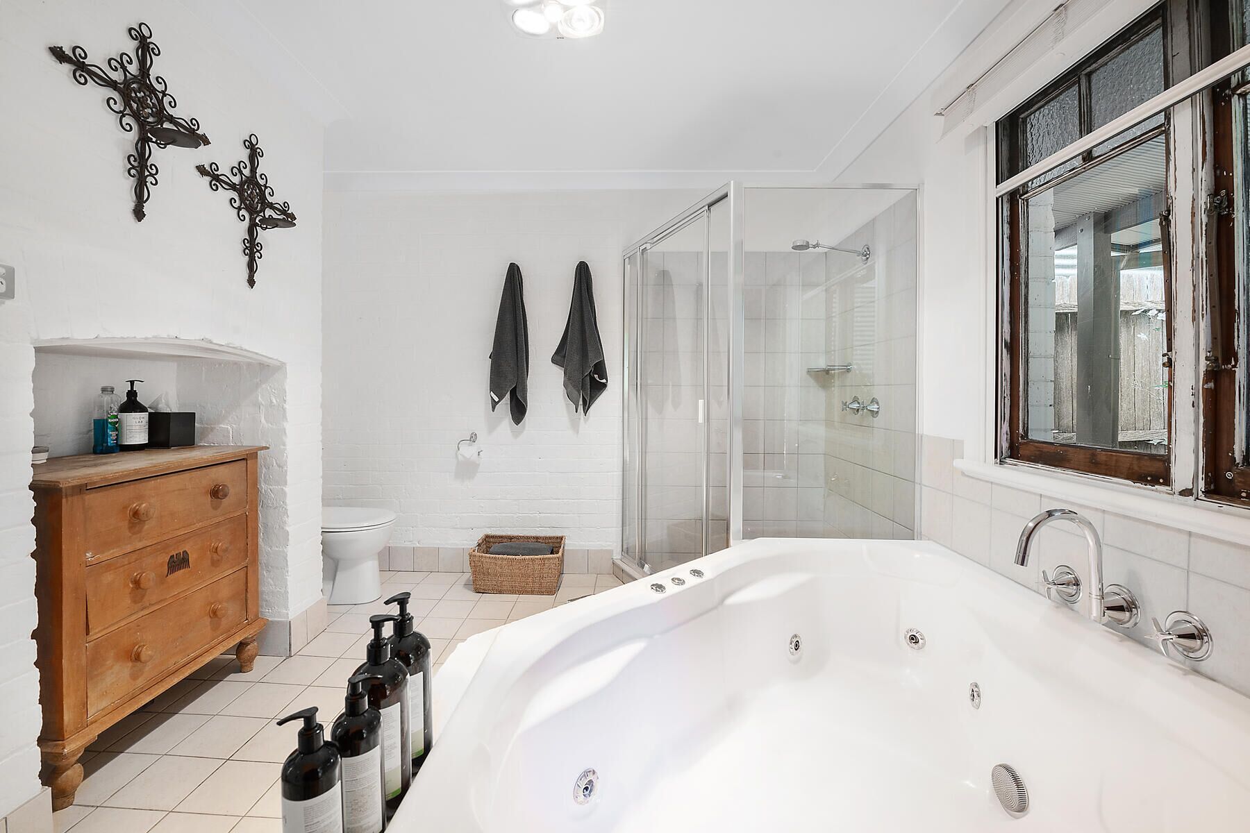 Een moderne badkamer met een witte badkuip, een houten wastafelmeubel, een glazen douchecabine en een raam met uitzicht.