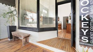 Une terrasse en bois avec un banc, une grande fenêtre avec des stores et une enseigne indiquant « Hockeys Guest Cottage ».