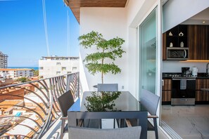 Un balcon avec une table en verre, des chaises et un arbre en pot.