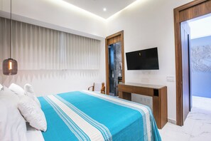 Une chambre moderne avec un lit, un bureau en bois, une télévision et une salle de bain visible à travers une porte en verre.