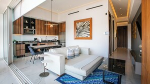 A modern living room with a sofa, coffee table, and a dining area with a kitchen in the background. - NEW Chic Condo with Scenic Views | Pool & Gym (Puerto Vallarta)