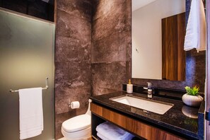 Une salle de bain moderne avec un mur en marbre, un lavabo sur un plan de toilette noir et un meuble-lavabo en bois.