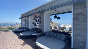A rooftop terrace with two round seating areas, a view of the cityscape, and a pool area. - NEW Chic Condo with Scenic Views | Pool & Gym (Puerto Vallarta)