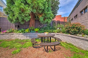 Enjoy dining or socializing in this patio area surrounded by lush greenery and a large tree.