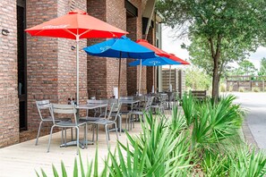 An outdoor seating area with tables and chairs, red and blue umbrellas, and a brick building. - Walk to the Beach, Brand New Luxe Beach House with Pool Access (Port St Joe)