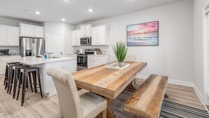 Una cocina moderna con armarios blancos, electrodomésticos de acero inoxidable y una mesa de comedor de madera con taburetes de bar.