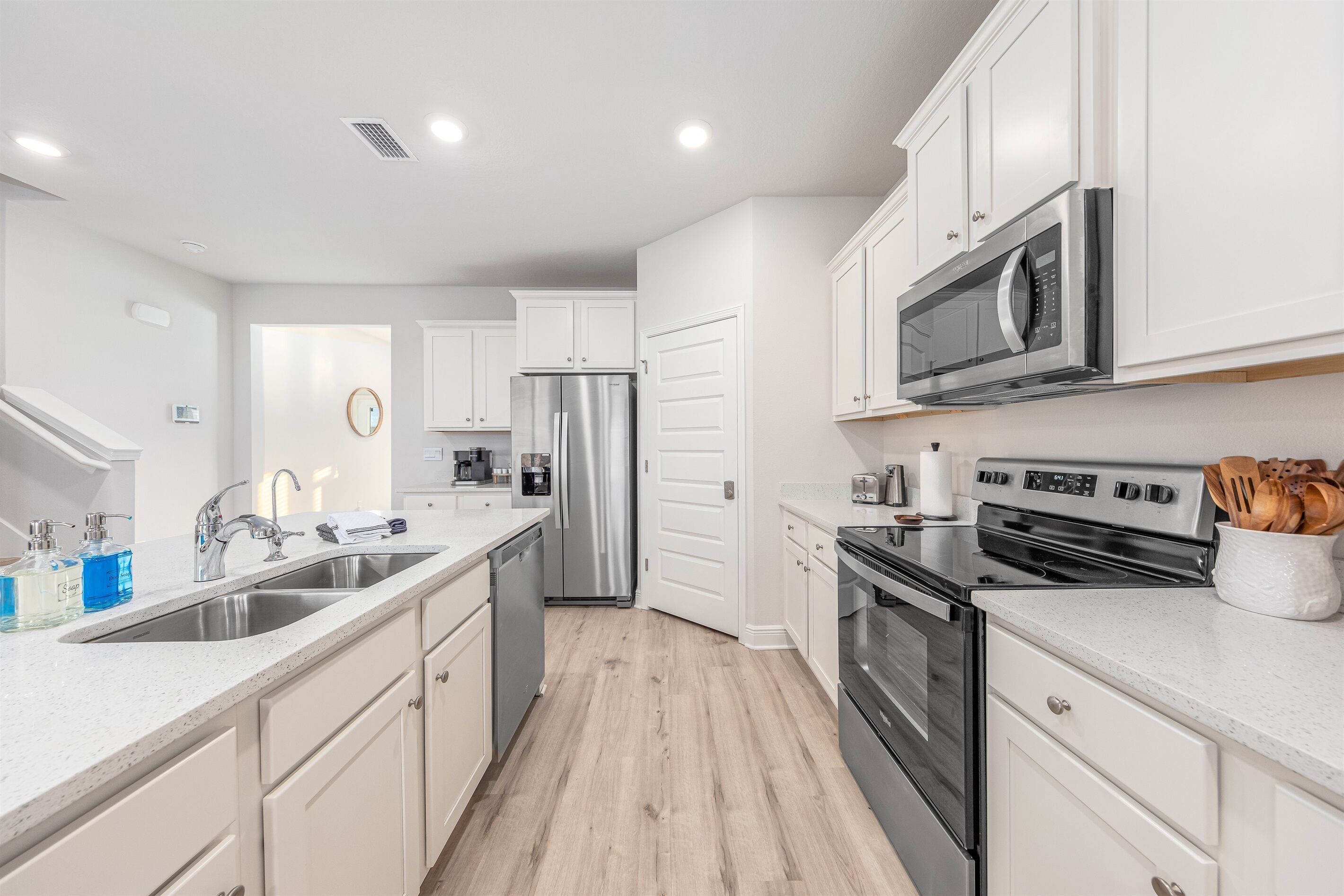 A modern kitchen with white cabinets, stainless steel appliances, and a wooden floor.