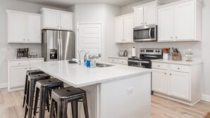 Una cocina moderna con armarios blancos, electrodomésticos de acero inoxidable y una isla central con taburetes.