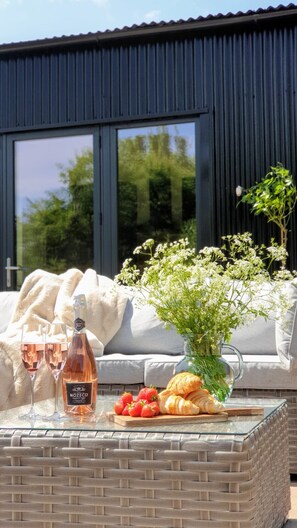 A modern outdoor seating area with a glass table, a bottle of wine, strawberries, and a vase of flowers.