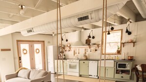 Een ruime woonkamer met een schommel, een bank en een keuken op de achtergrond.