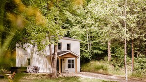 Een tweelaags huis met een veranda, omringd door bomen en een gazon.