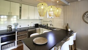 Una cocina moderna con armarios blancos, encimera oscura y tres lámparas colgantes de mimbre.