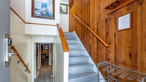 Un escalier avec des rampes en bois et une main courante en métal, menant à une pièce d’où l’on peut admirer un jardin.