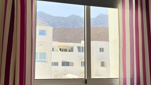 A window with striped curtains, a view of buildings, and mountains in the background. - 2BR Home - 3 min to Agaete Beach - Pool (Agaete)