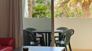 A balcony with a table and chairs, a red sofa, and a view of palm trees and buildings. - 2BR Home - 3 min to Agaete Beach - Pool (Agaete)