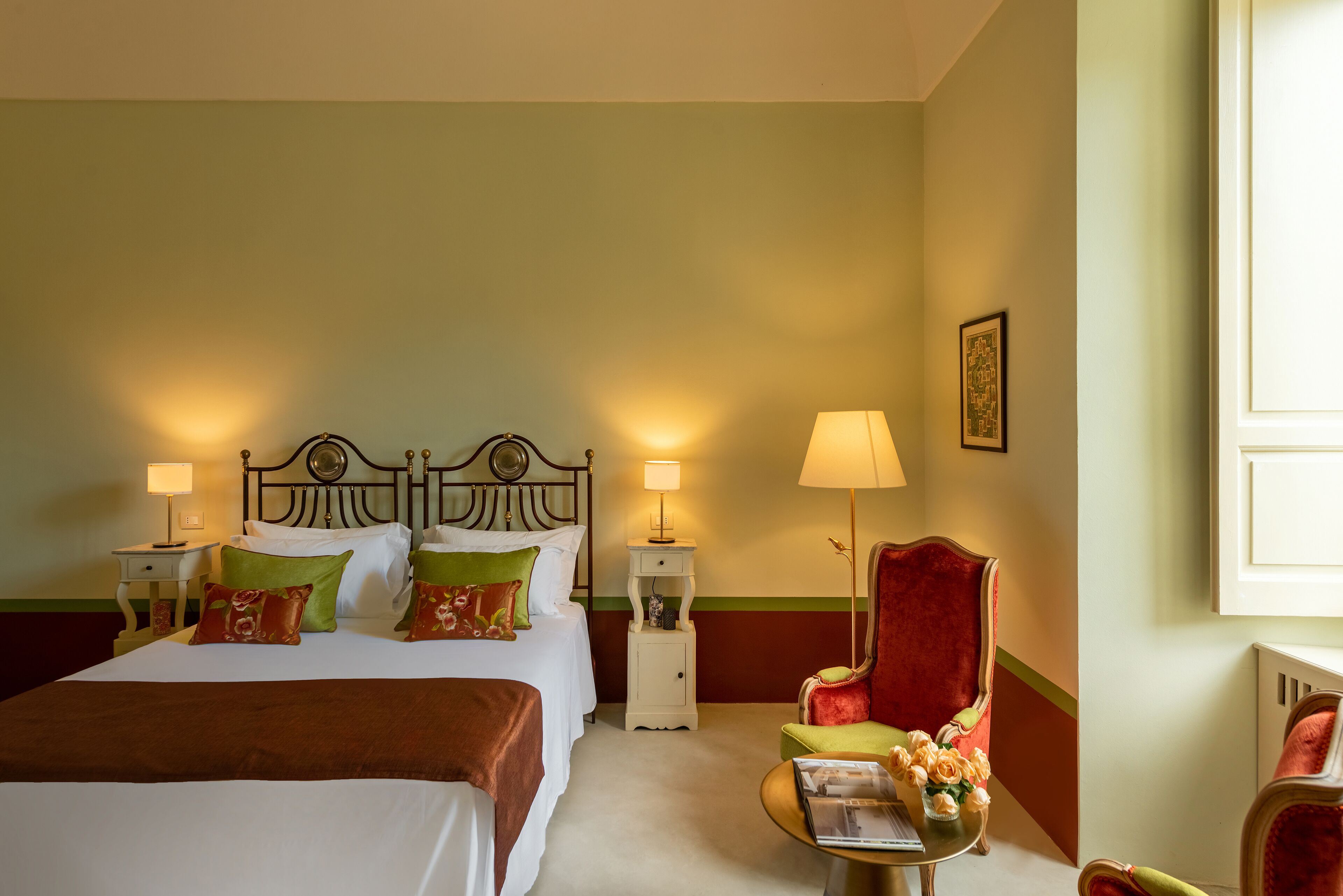 A hotel room with a bed, two bedside tables, a chair, and a small table with a vase of flowers.