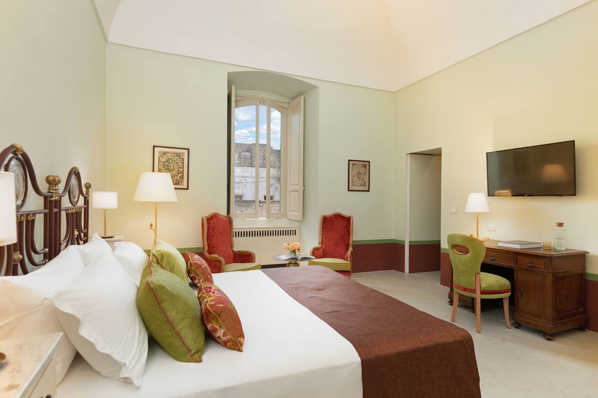 Ein Hotelzimmer mit einem Bett, zwei Stühlen, einem Schreibtisch, einem Fernseher und einem Fenster.