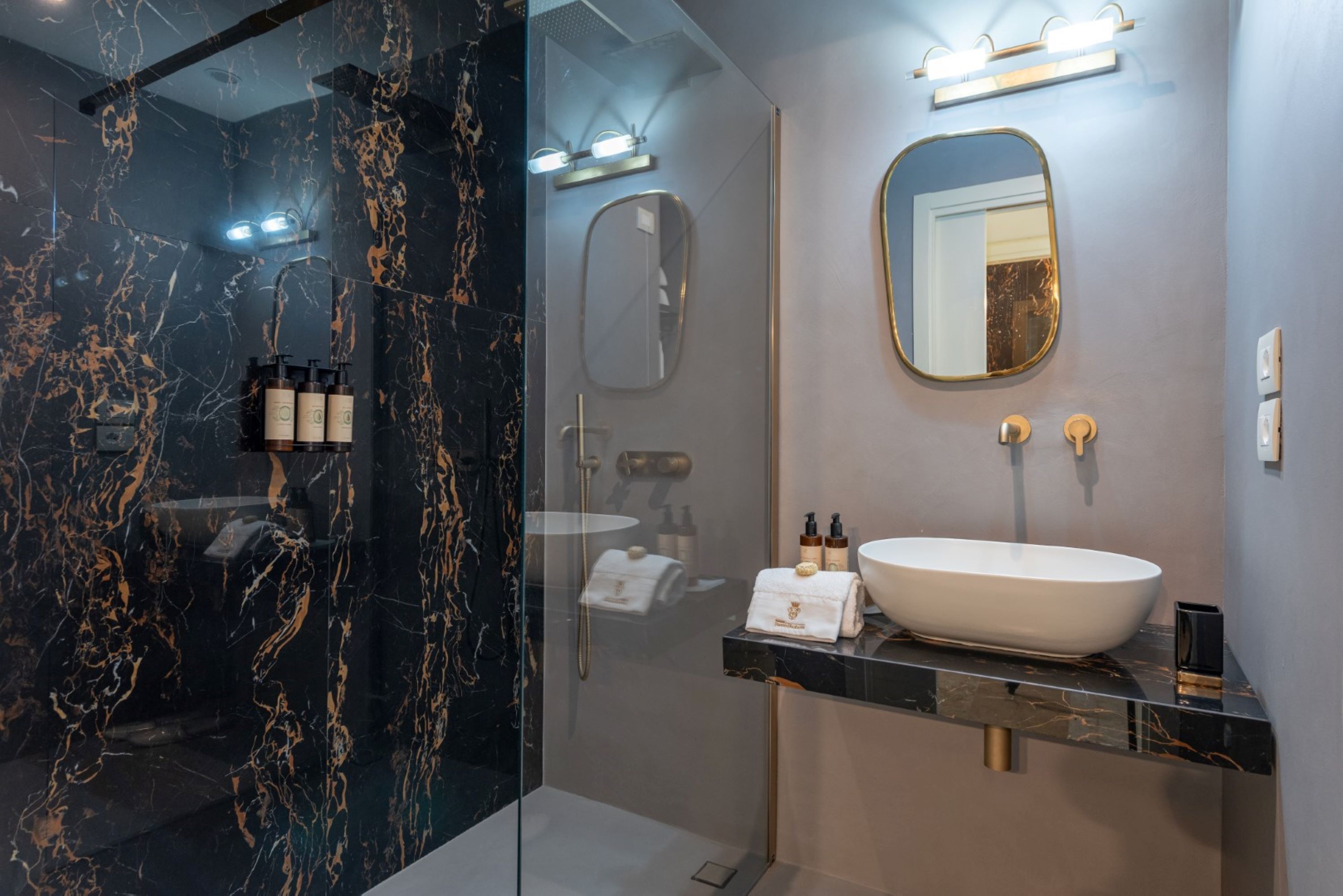 A modern bathroom with a glass-enclosed shower, a marble-tiled wall, a white sink, and a mirror.