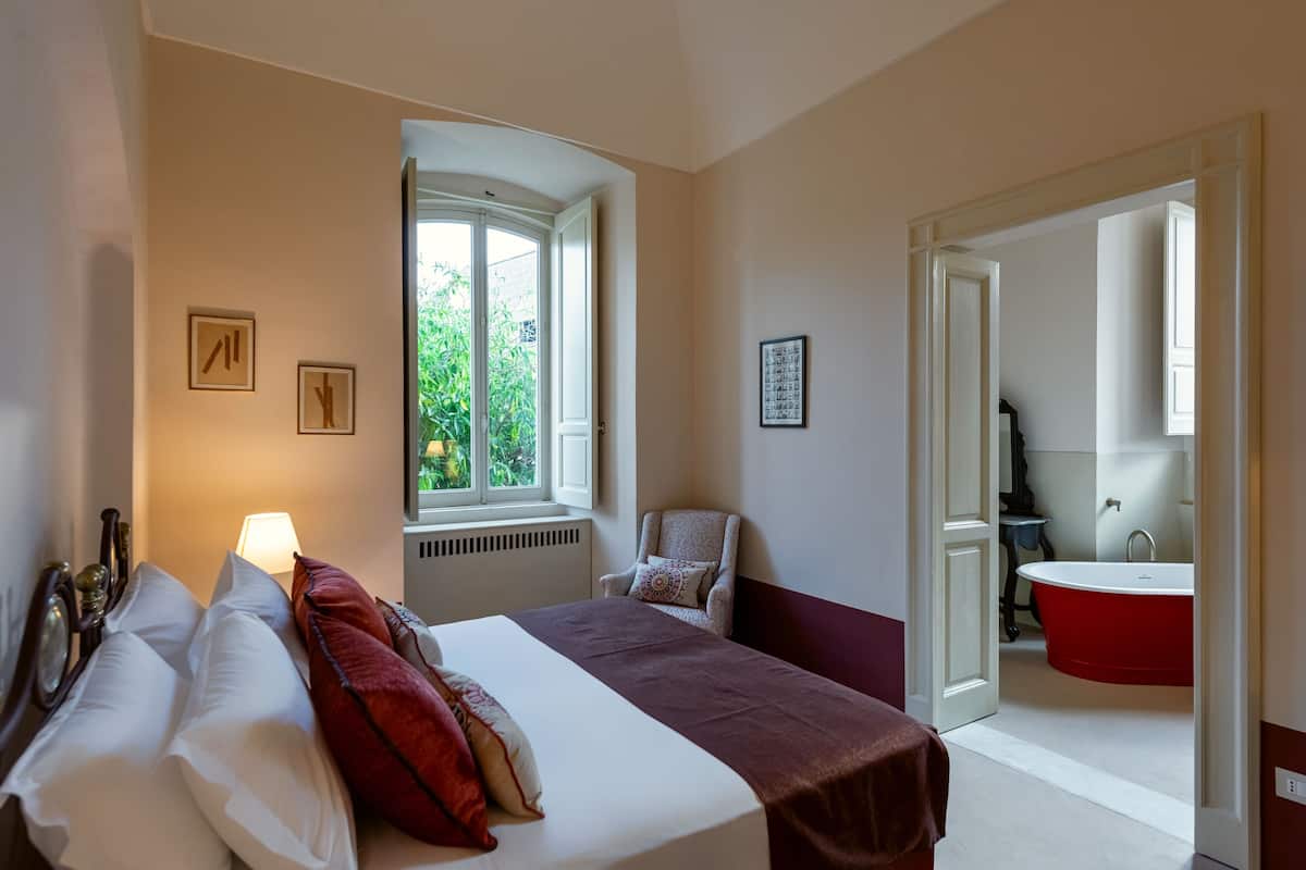 Ein Hotelzimmer mit Bett, Fenster, Sessel und einer roten Badewanne.