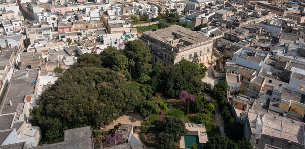 Vista aérea de una zona urbana densamente poblada, con un edificio destacado rodeado de exuberante vegetación y un pequeño patio.