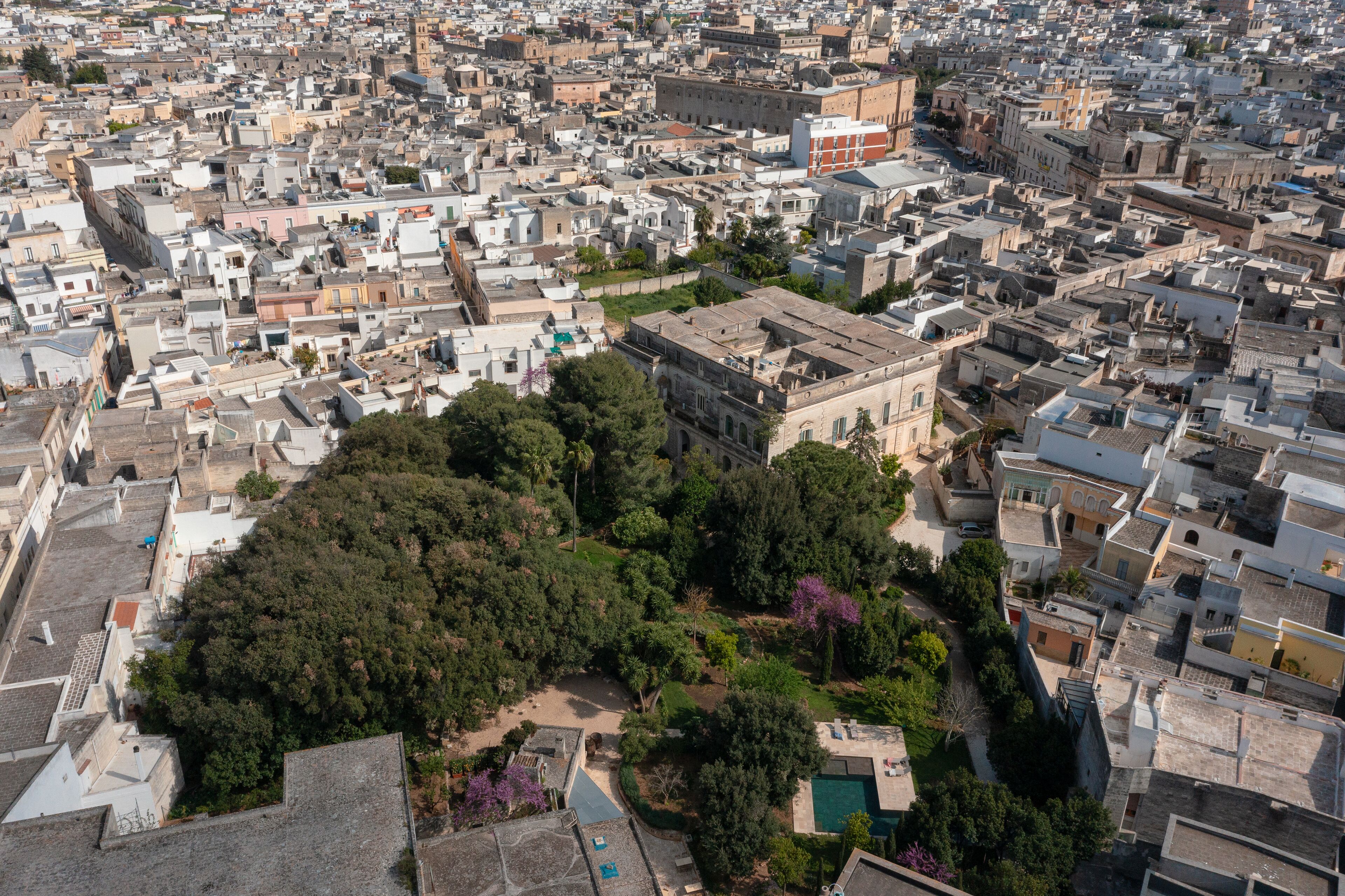 Vista aérea de una zona urbana densamente poblada con edificios residenciales y comerciales, rodeada de vegetación y un espacio abierto central.