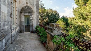 A stone building with a door, a small porch, and a garden with trees and plants. - Palazzo Donna Elisabetta -Guest House (Manduria)
