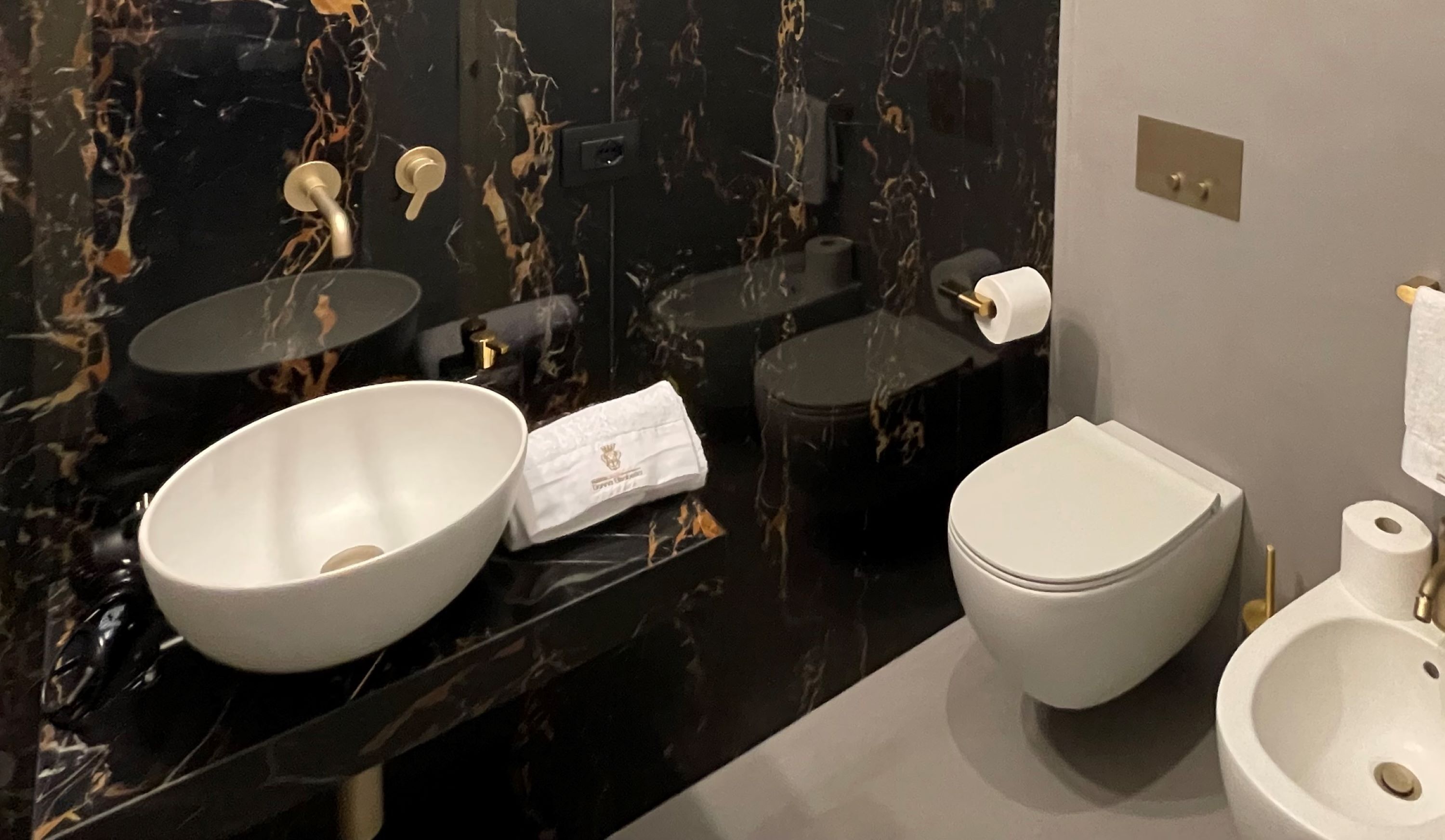 Une salle de bain moderne avec un meuble-lavabo en marbre noir, un lavabo blanc, des toilettes et un bidet.