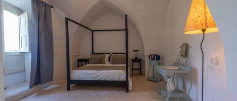 Una cama con dosel, una mesita de noche, una mesa con lámpara y una ventana con cortinas.