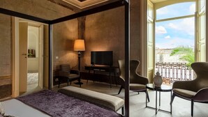 A hotel room with a bed, a desk with a lamp, two chairs, and a balcony with a view. - Palazzo Donna Elisabetta -Guest House (Manduria)