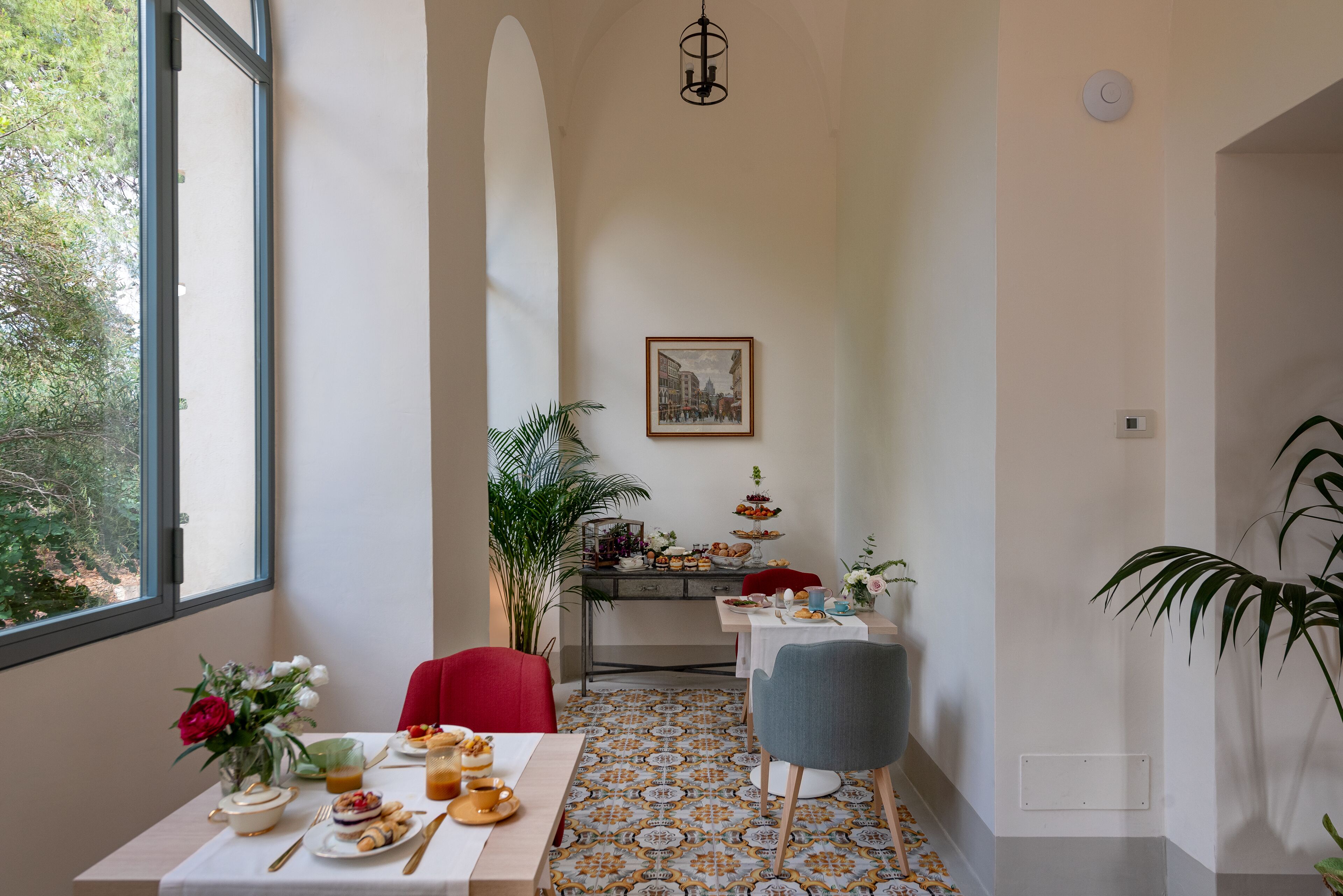 A dining area with a table set for breakfast, a red chair, a grey chair, and a potted plant.