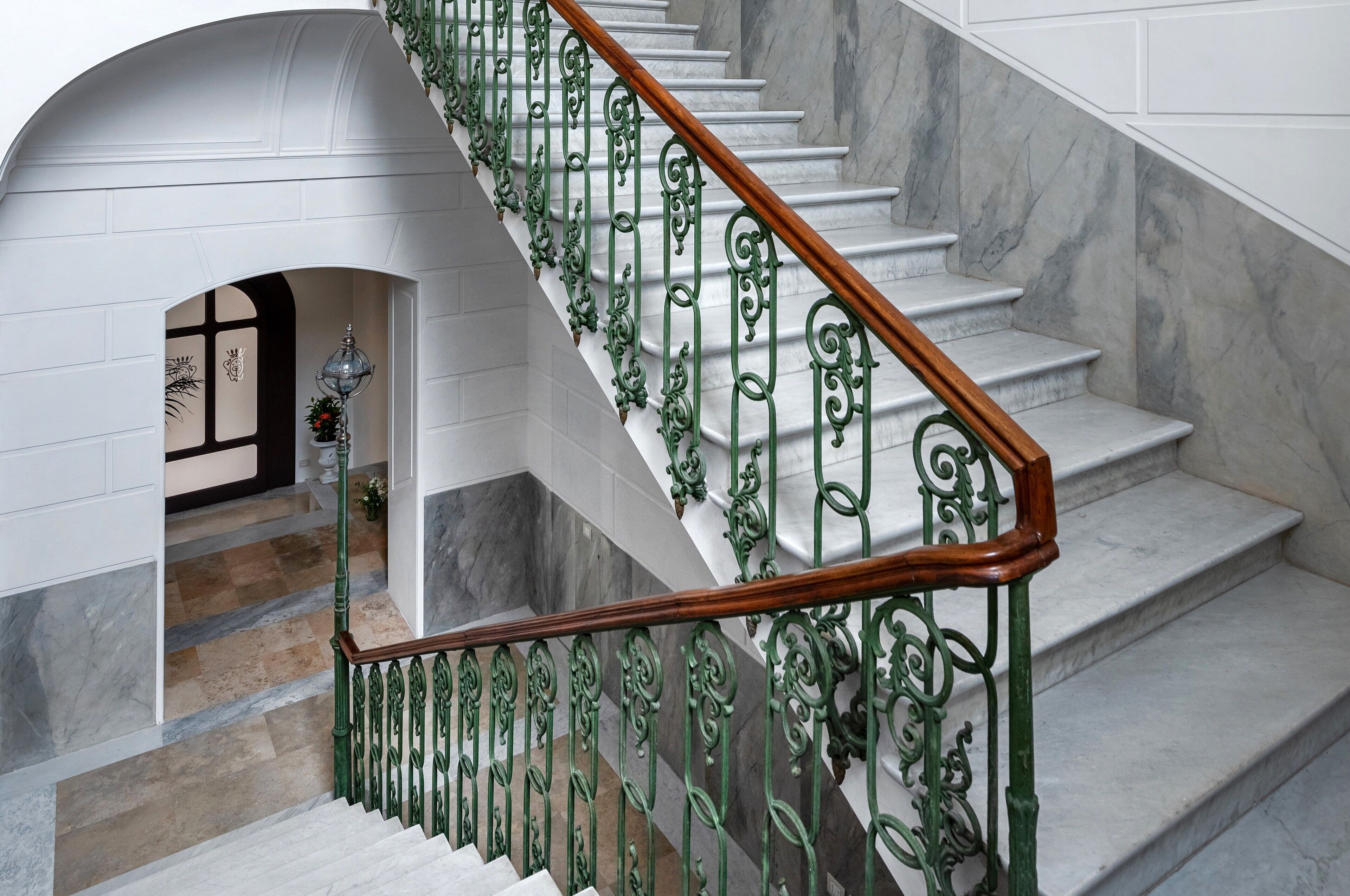 A marble staircase with ornate green metal railings and a wooden handrail.