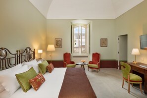 Una habitación de hotel con cama, dos sillas, un escritorio, una lámpara y una ventana.
