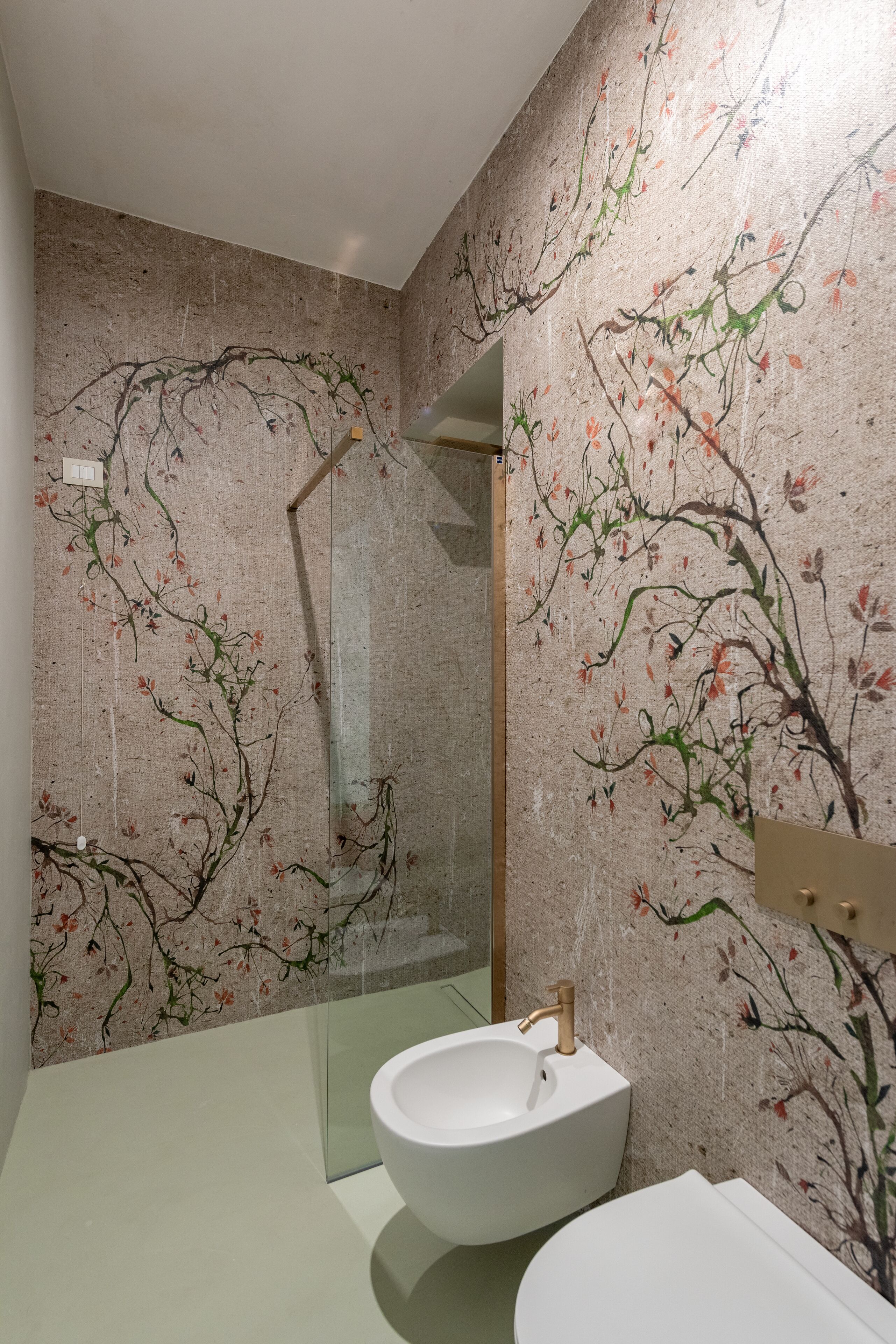 Une salle de bain avec un lavabo blanc, un miroir et un mur orné d’un motif floral.