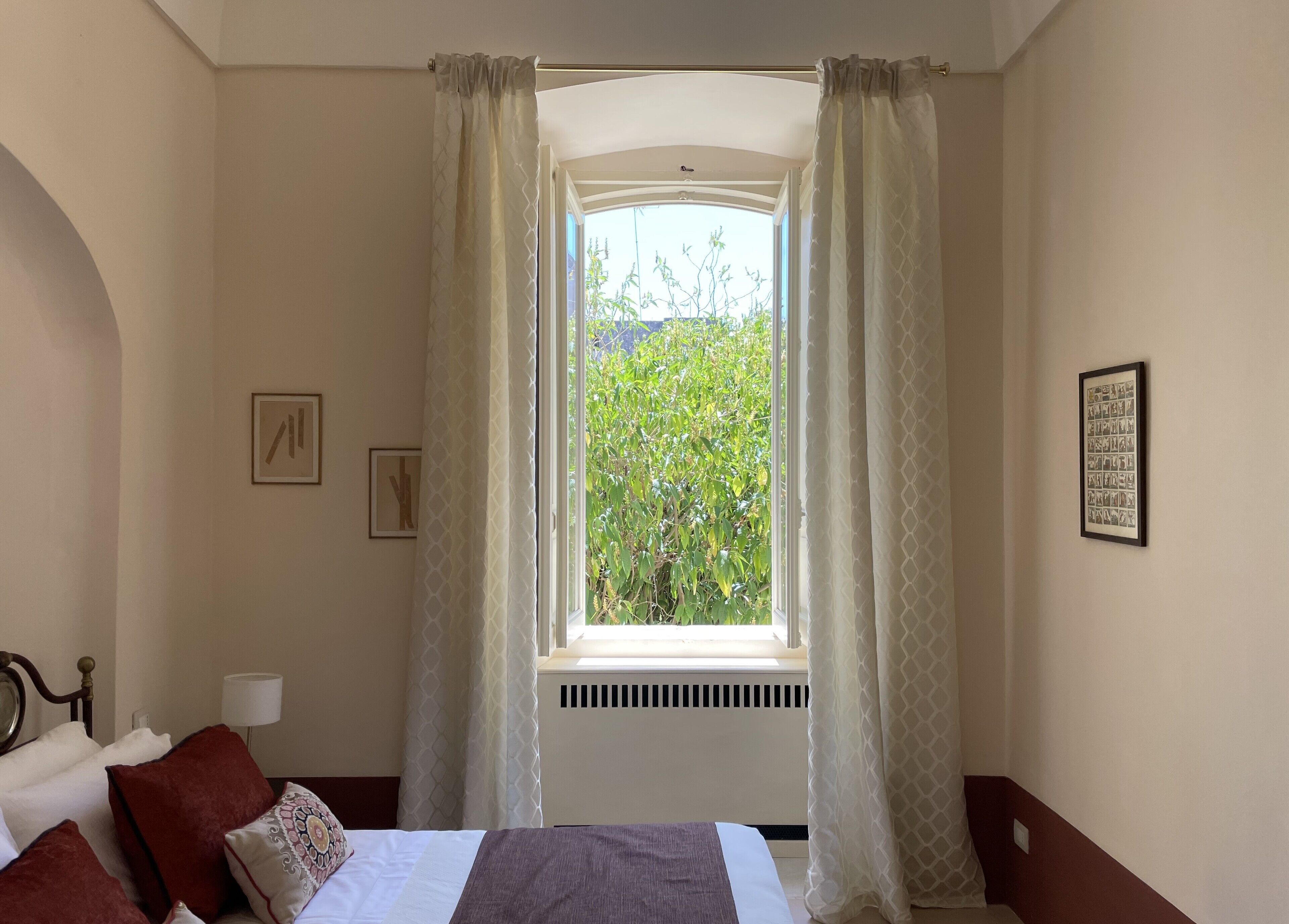 A bedroom with a bed, a window with curtains, a radiator, and a wall-mounted picture.