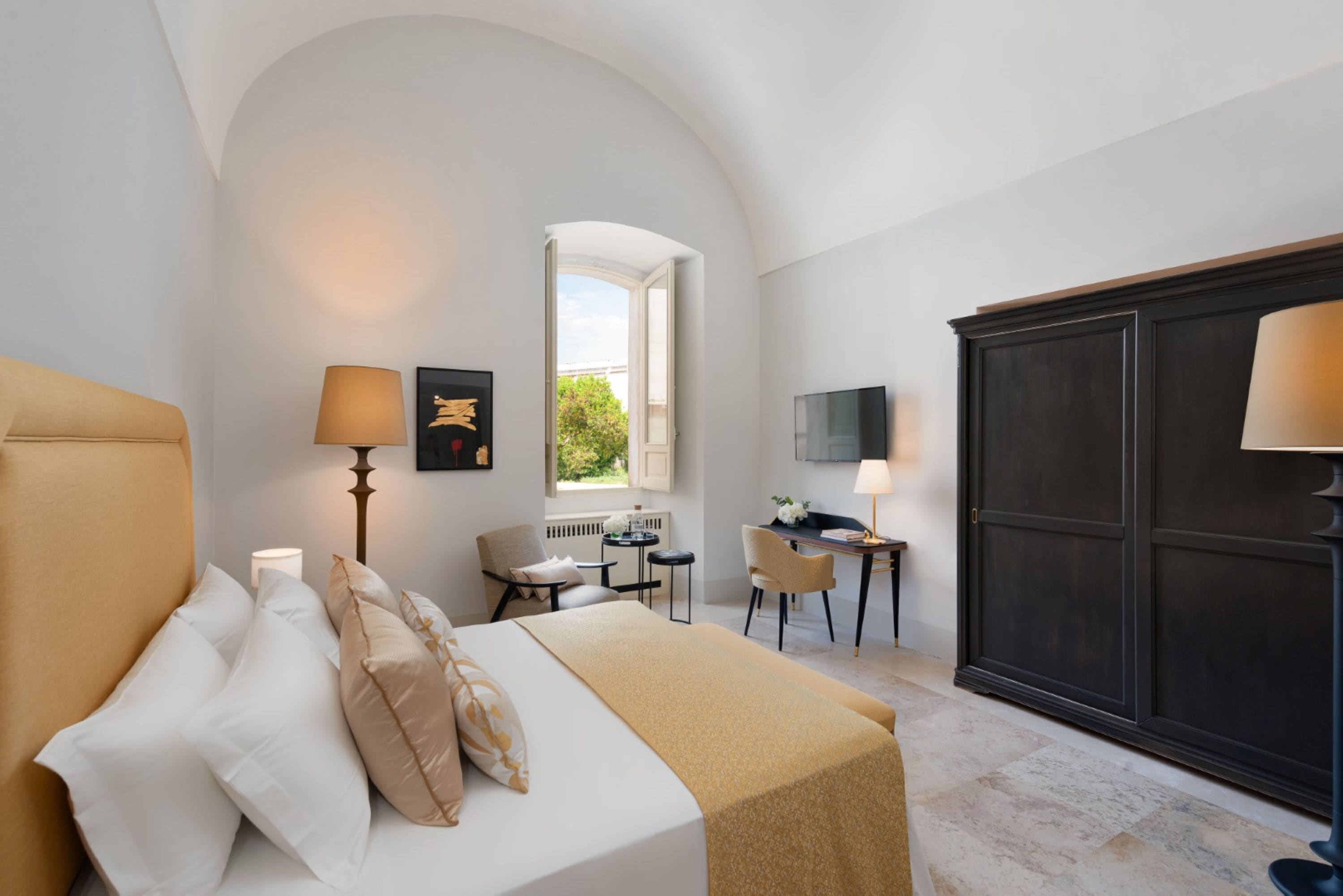 Quarto com cama, luminárias de cabeceira, escrivaninha e guarda-roupa.