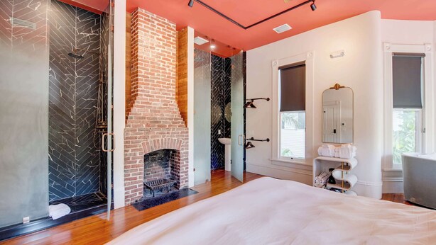 A bedroom with a brick fireplace, a glass shower enclosure, and a large bed.