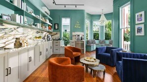 A modern kitchen with white cabinets, a marble countertop, and a dining area with orange chairs and a blue sofa set.