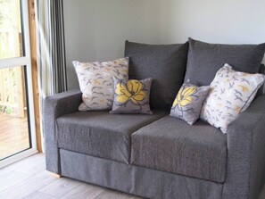 A grey sofa with three cushions featuring a bird and flower pattern, positioned against a wall with a window. - Longtails, beautiful lodge retreat Bantham S.Devon (Bantham)