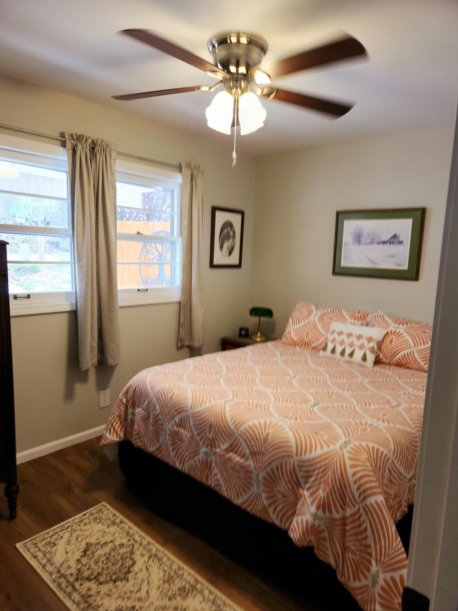 A bedroom with a bed, a ceiling fan, a window with curtains, and a rug.