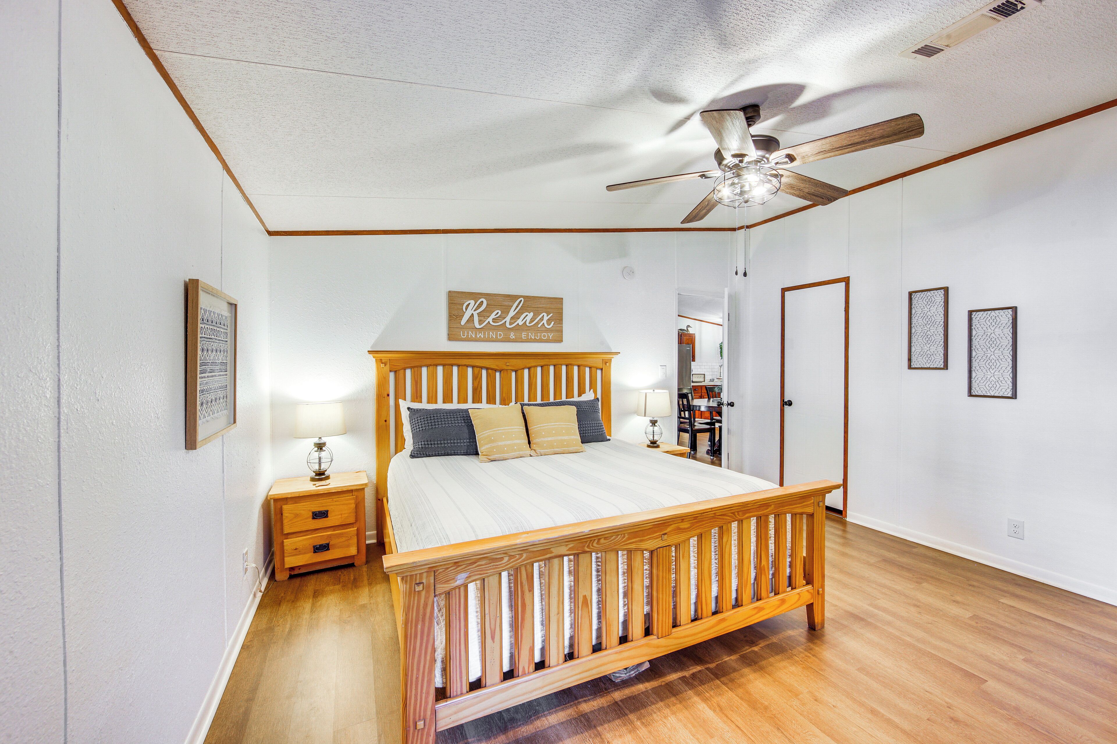 Una camera da letto con un letto di legno, un comodino, una ventola a soffitto e un cartello appeso al muro.