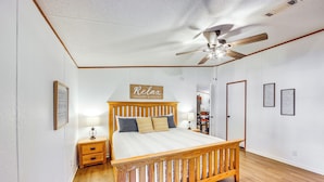 Un dormitorio con cama de madera, mesita de noche, ventilador de techo y un letrero en la pared.