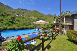 A swimming pool with lounge chairs, a wooden fence, and a building with a stone facade. - Casa Le Meriche (Castiglione di Garfagnana)